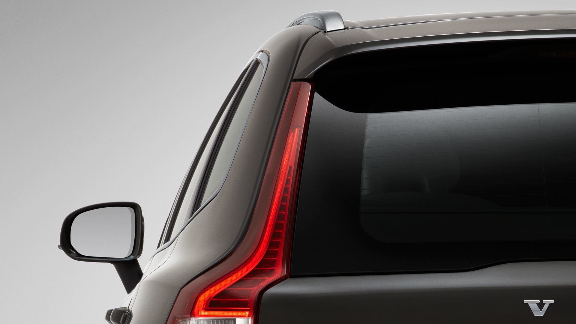 Primer plano de la parte trasera izquierda de un vehículo Volvo, destacando la luz trasera, la luneta trasera y el emblema de Volvo.