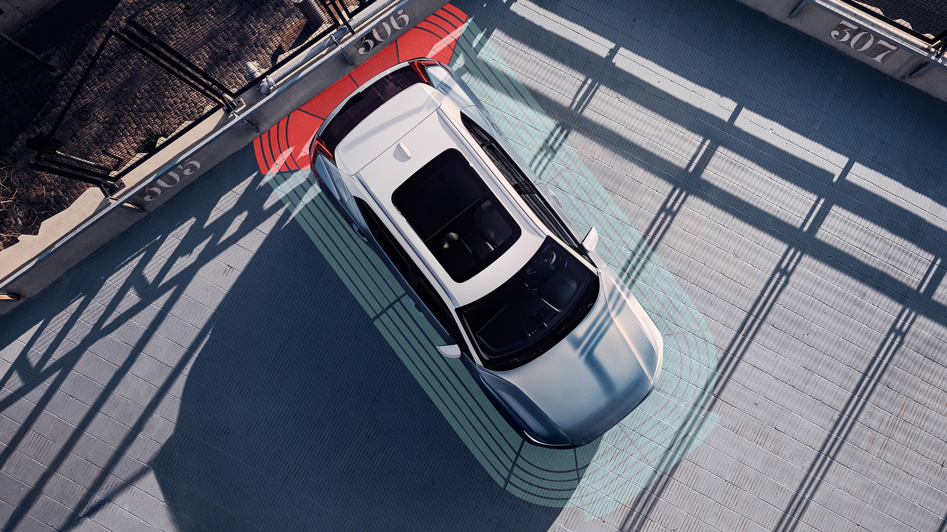 Overhead view of a Volvo vehicle in a parking space, displaying colored sensor zones around the car to illustrate its parking assistance technology.