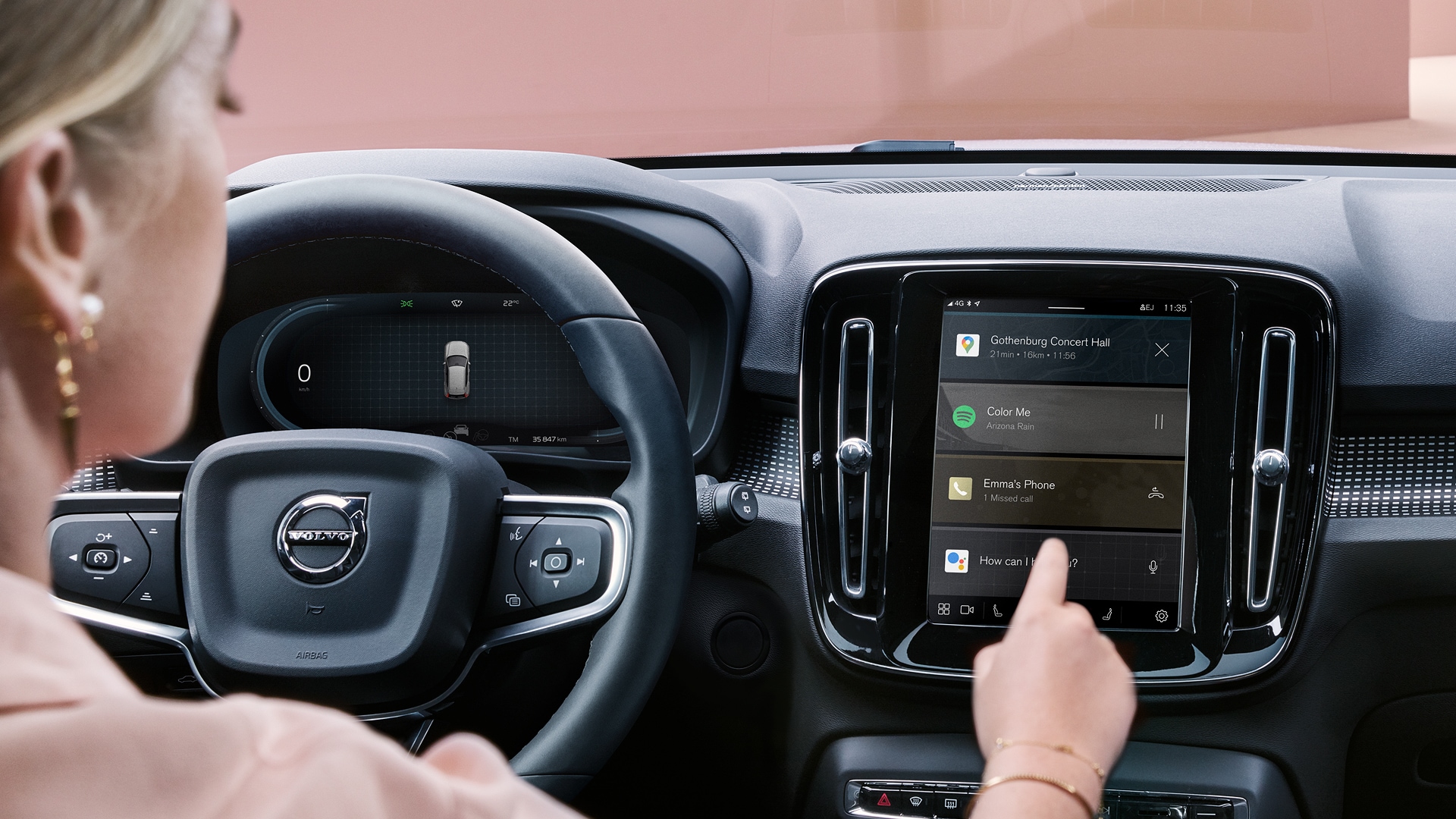 Close-up of a person using the touchscreen infotainment system in a Volvo car, displaying navigation, music, and phone notifications.